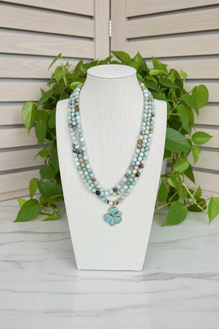 A multi-strand beaded necklace displayed on a cream fabric mannequin bust, set on a dark wooden table with green plants in the background.