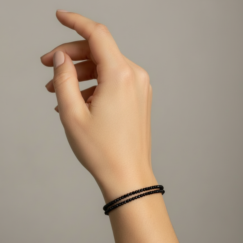 Hand wearing a black beaded bracelet on a neutral background