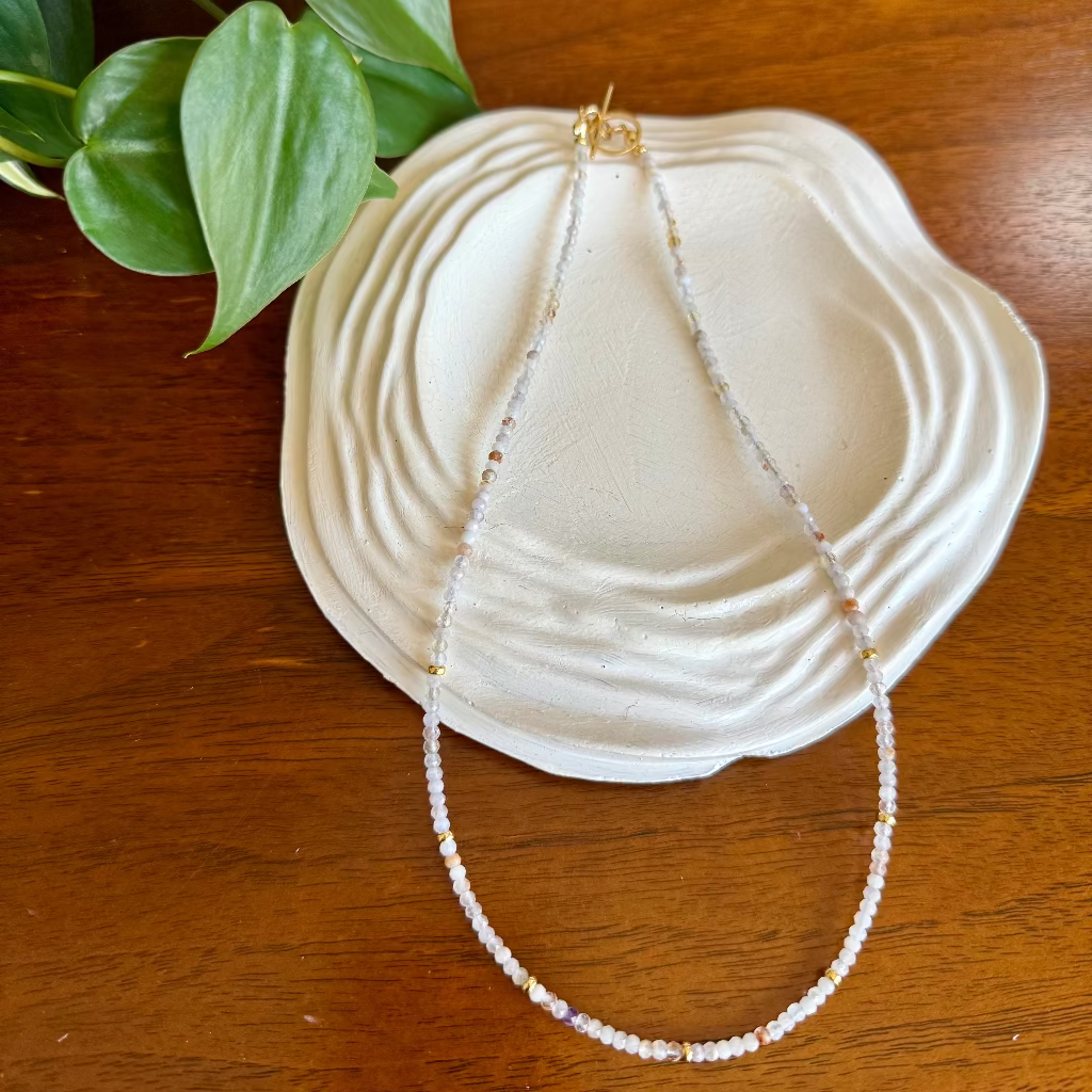 Pearl necklace on a white shell with green leaves on a wooden surface