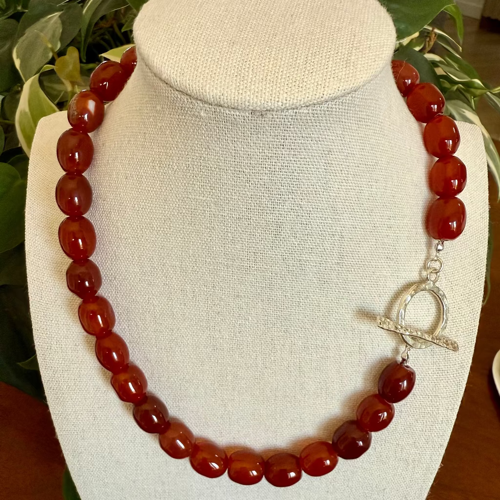 Carnelian beaded necklace with a silver heart clasp on a white bust