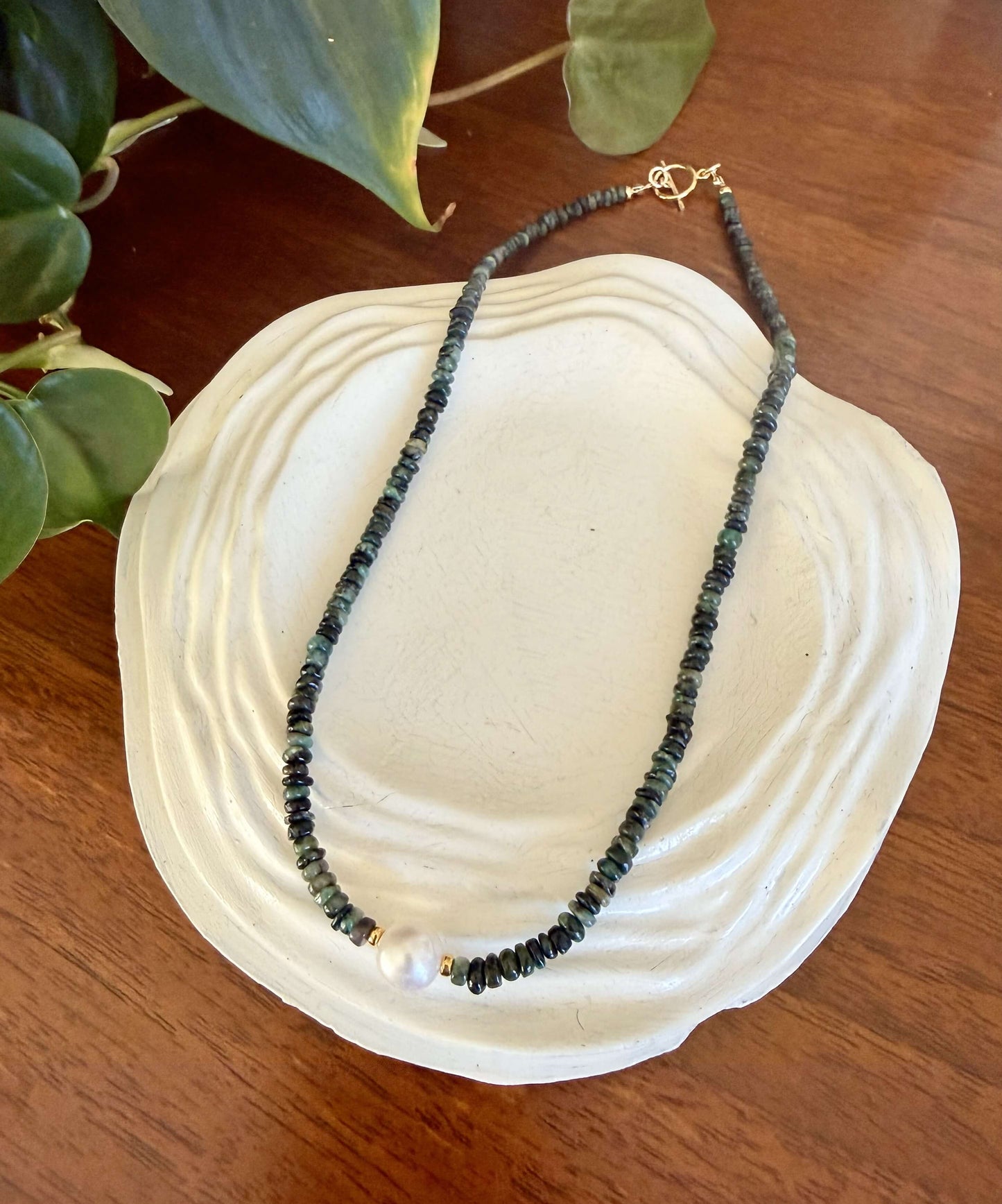 Necklace with green emerald beads and a pearl on a white shell against a wooden background