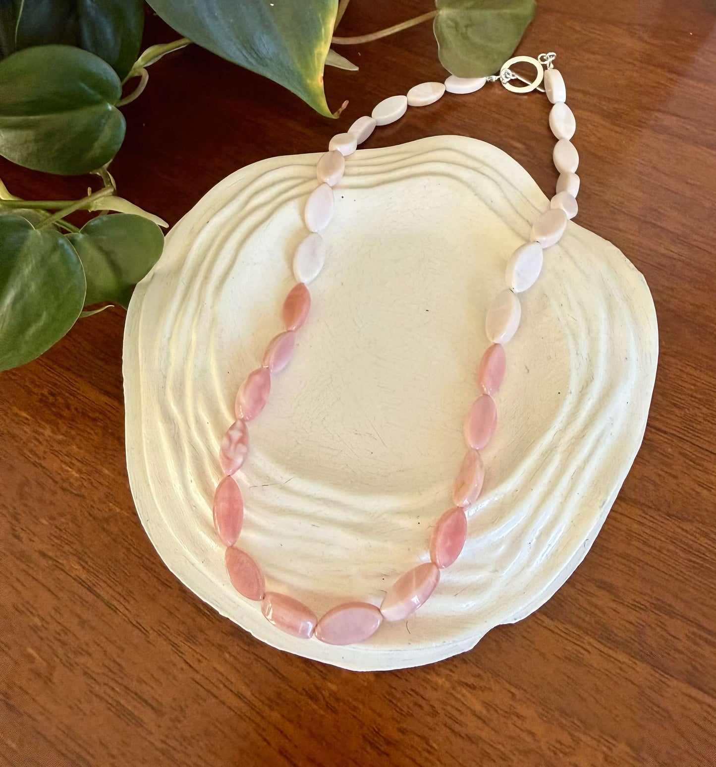 Necklace with pink beads on a large shell with green leaves in the background