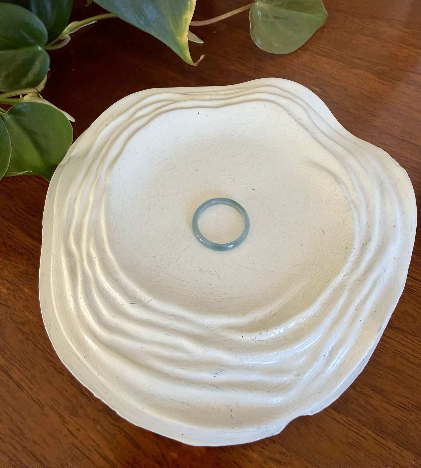 Thin green jade ring on a decorative white dish with a plant in the background