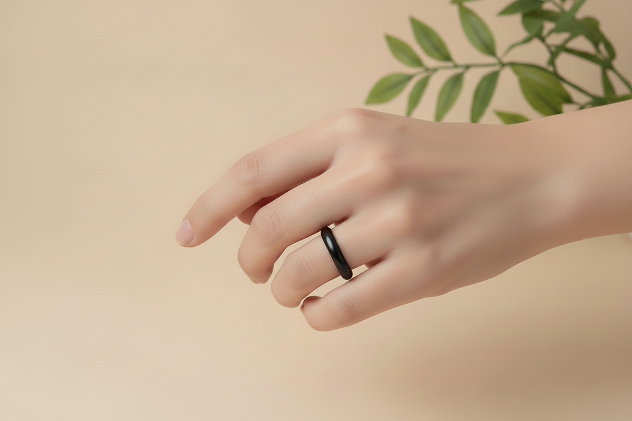 Hand wearing a black jade ring on a beige background with green leaves.