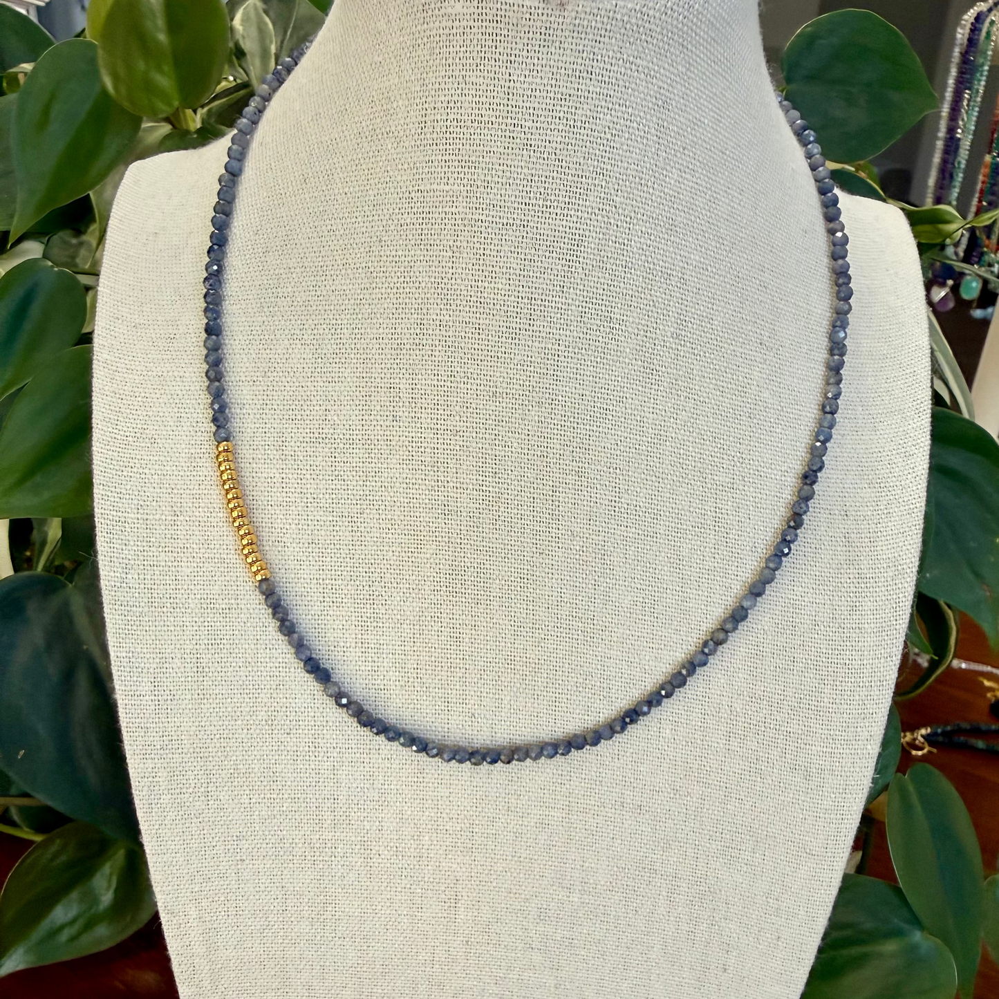 Sapphire necklace on a mannequin bust with green plants in the background