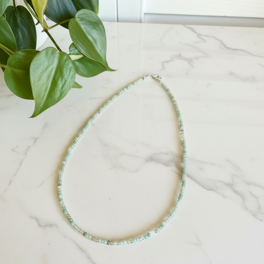 Necklace on a marble surface with a plant in the corner