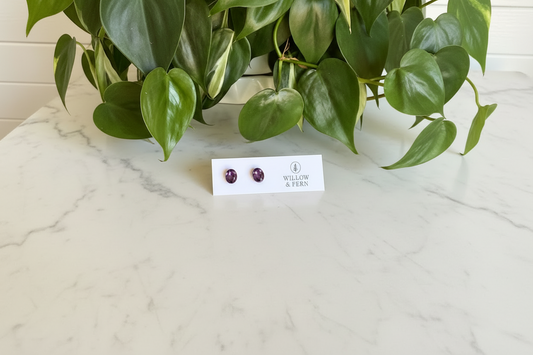 Pair of Amethyst earrings on a 'Willow & Fern' card on a white countertop with green leaves in the background