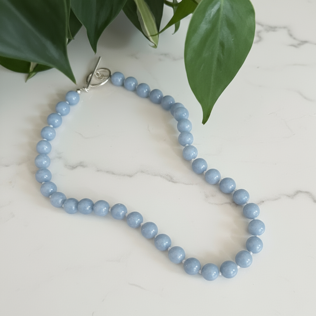 Willow & Fern Blue Angelite beaded gemstone necklace on a marble surface with green leaves in the background