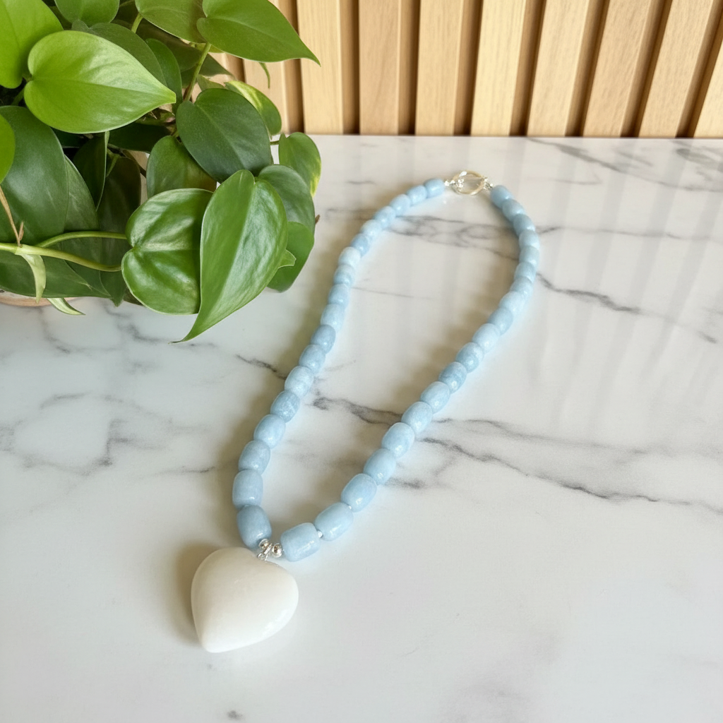 Necklace with light blue beads and a white pendant on a wooden surface with a plant in the background.
