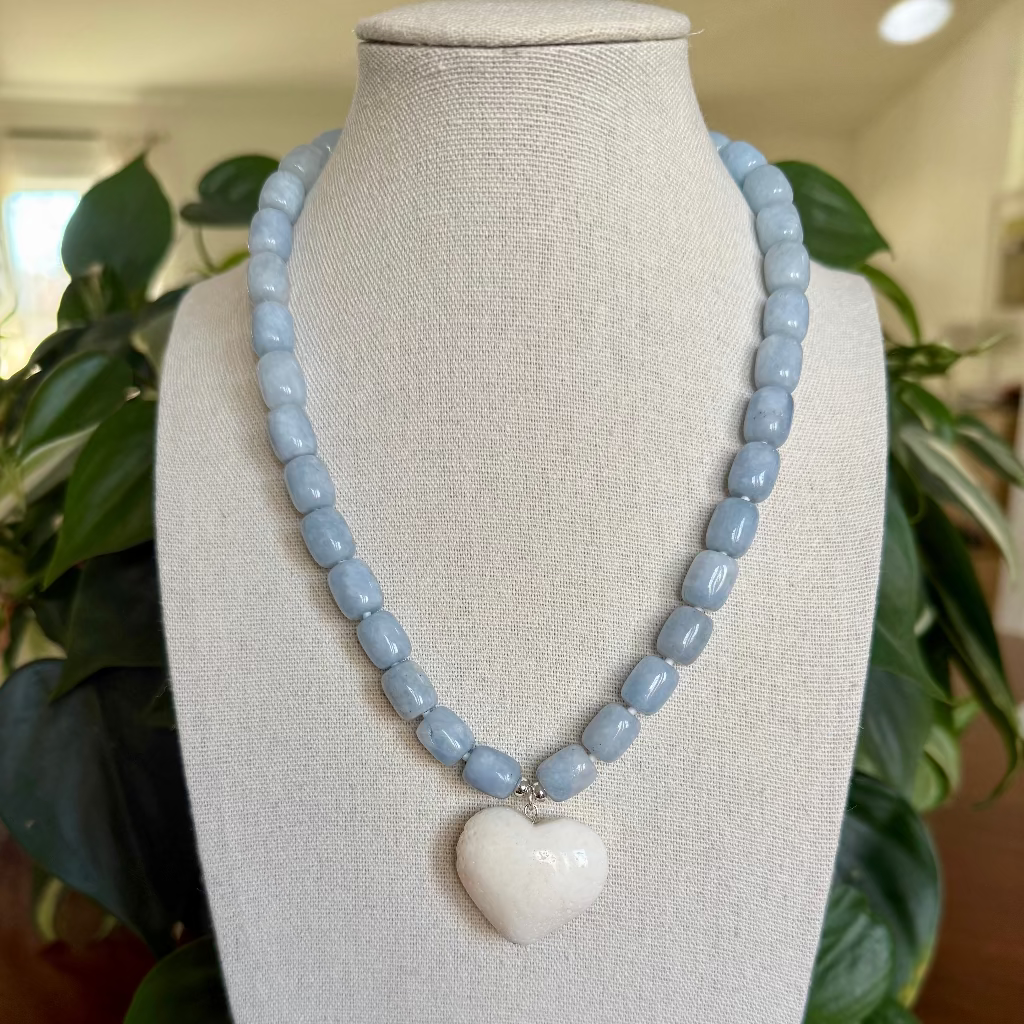 Necklace with blue beads and a heart-shaped white pendant on a mannequin bust.