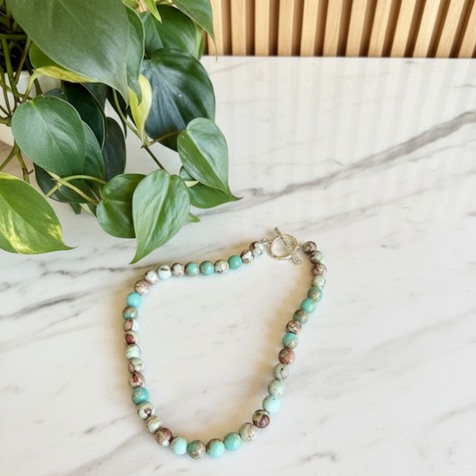 Multi colored necklace on a white countertop with a plant in the background