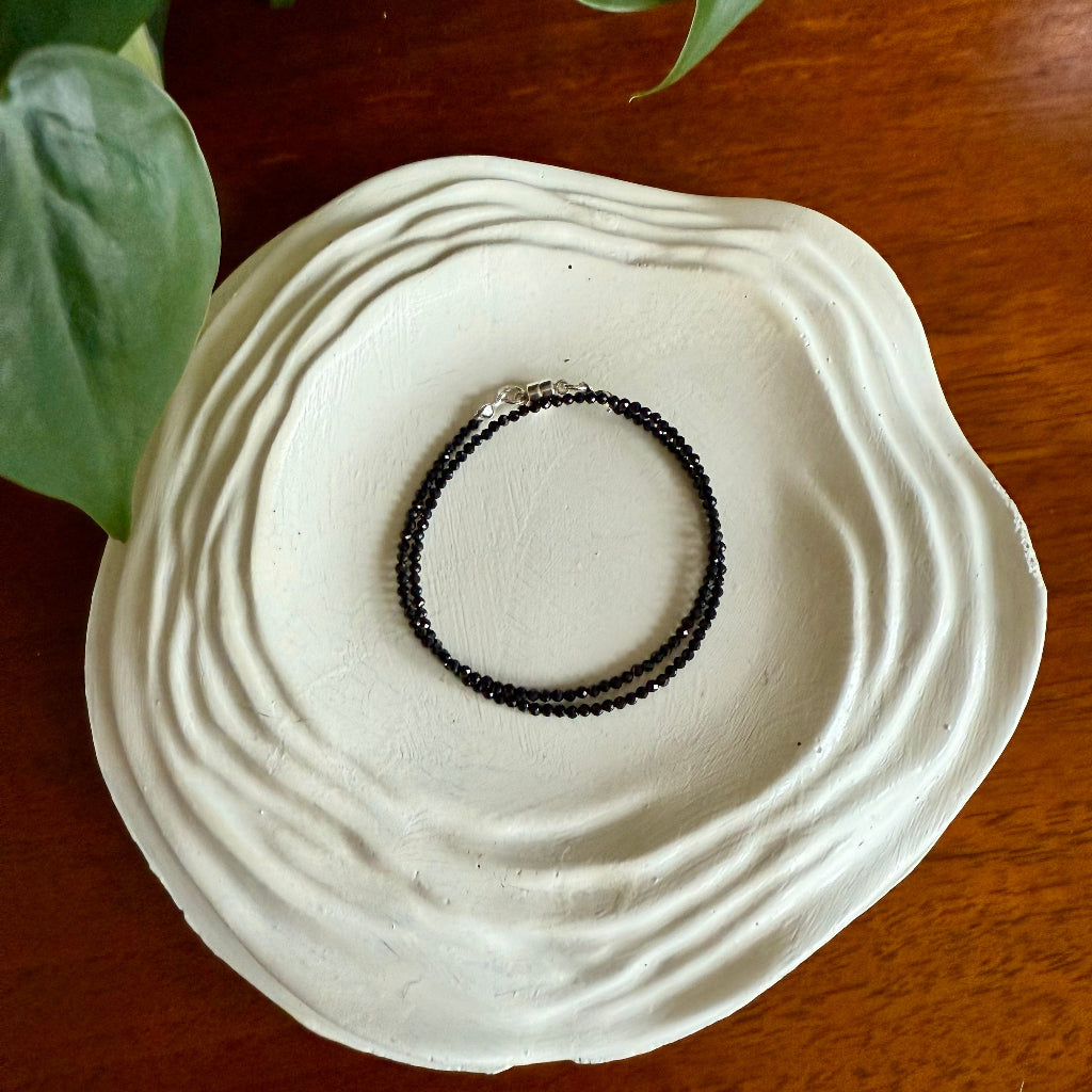 Black beaded bracelet on a white ceramic dish with green leaves in the background