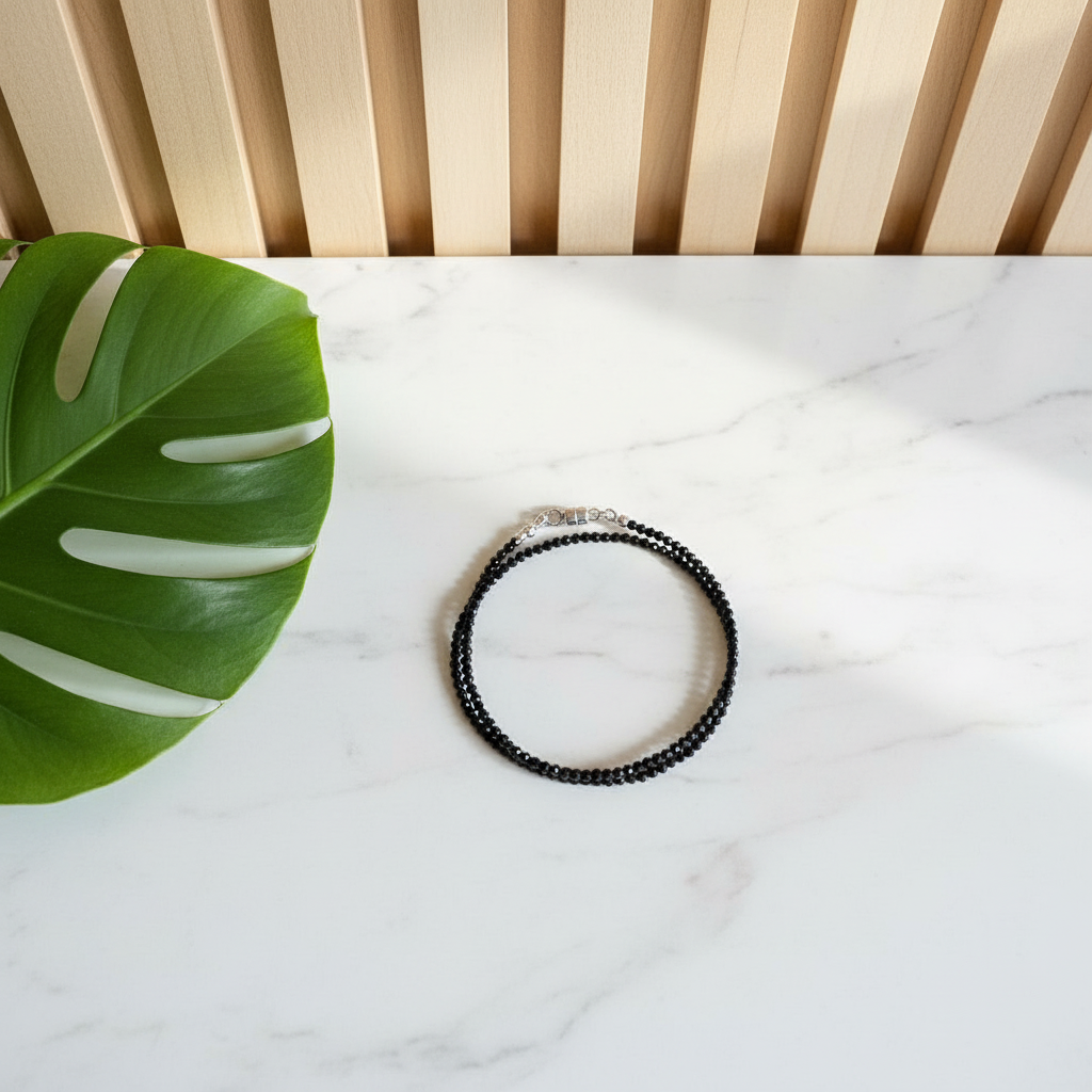 Black beaded bracelet on a marble surface with a green leaf and wooden slats in the background
