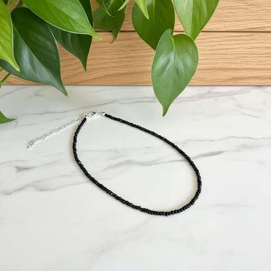 black beaded necklace on a white counter with a plant in the background