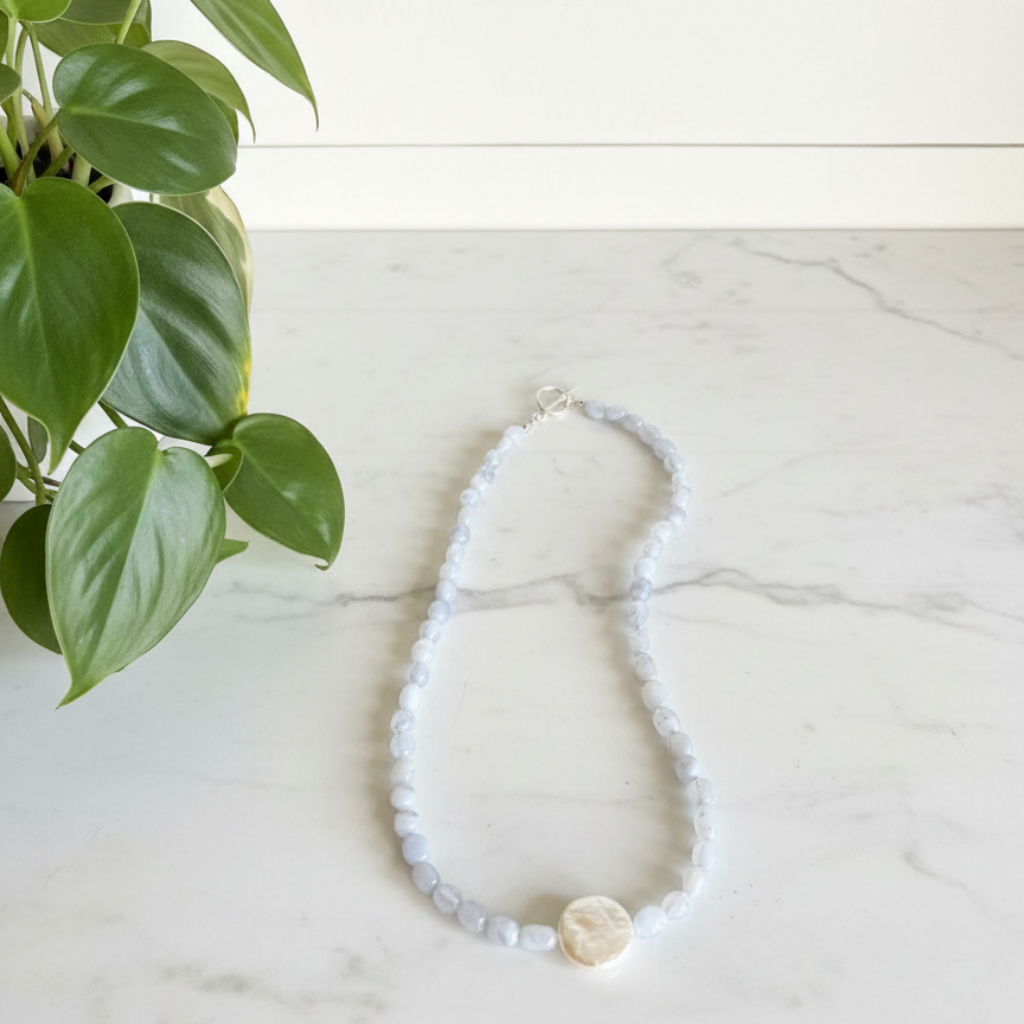 Beaded necklace with a pearl pendant on a marble surface next to a plant