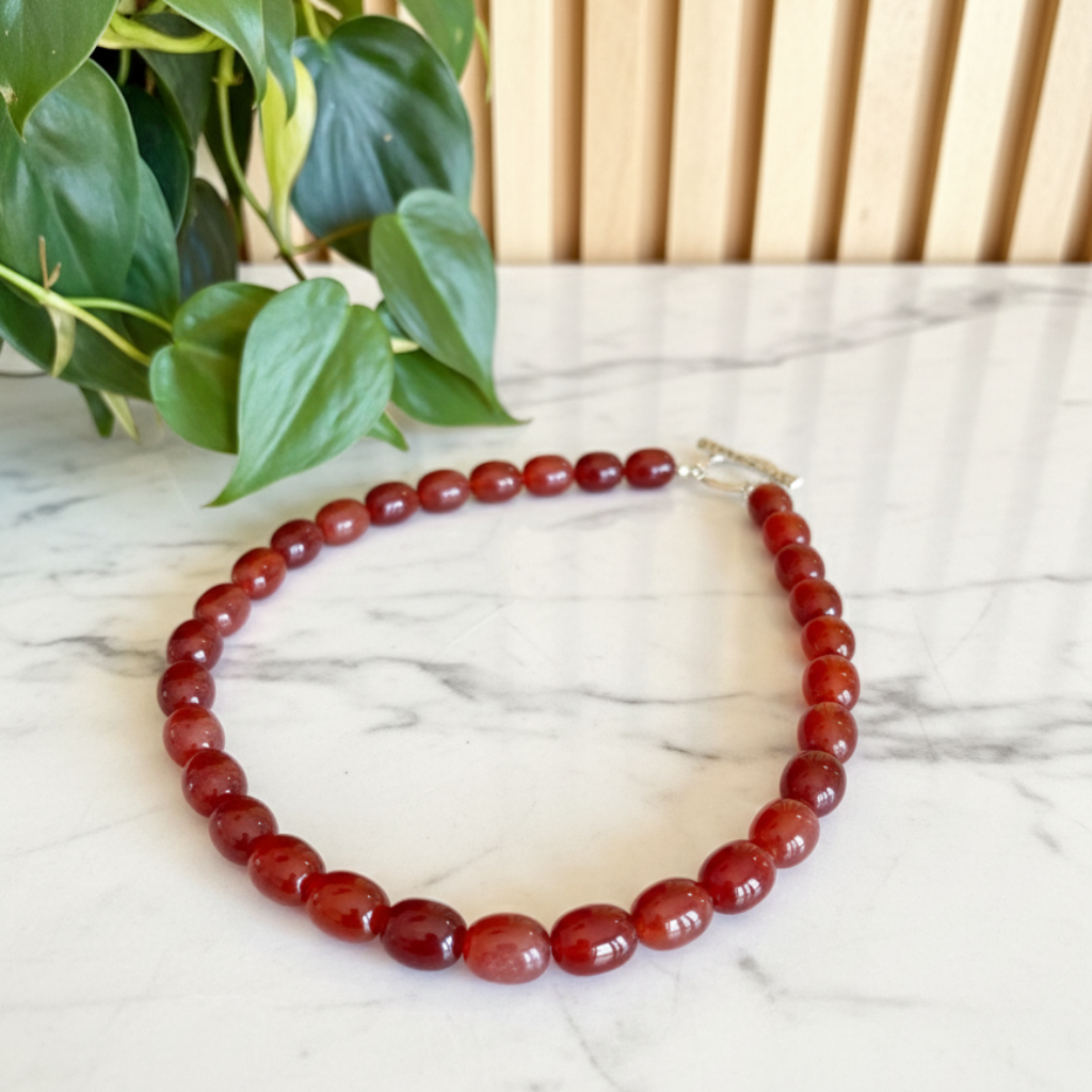 red beaded necklace on a white marble counter with a plant in the background