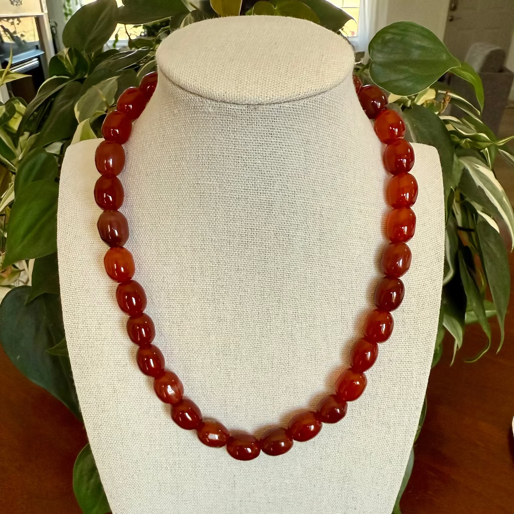 Red beaded necklace on a white bust with green plants in the background