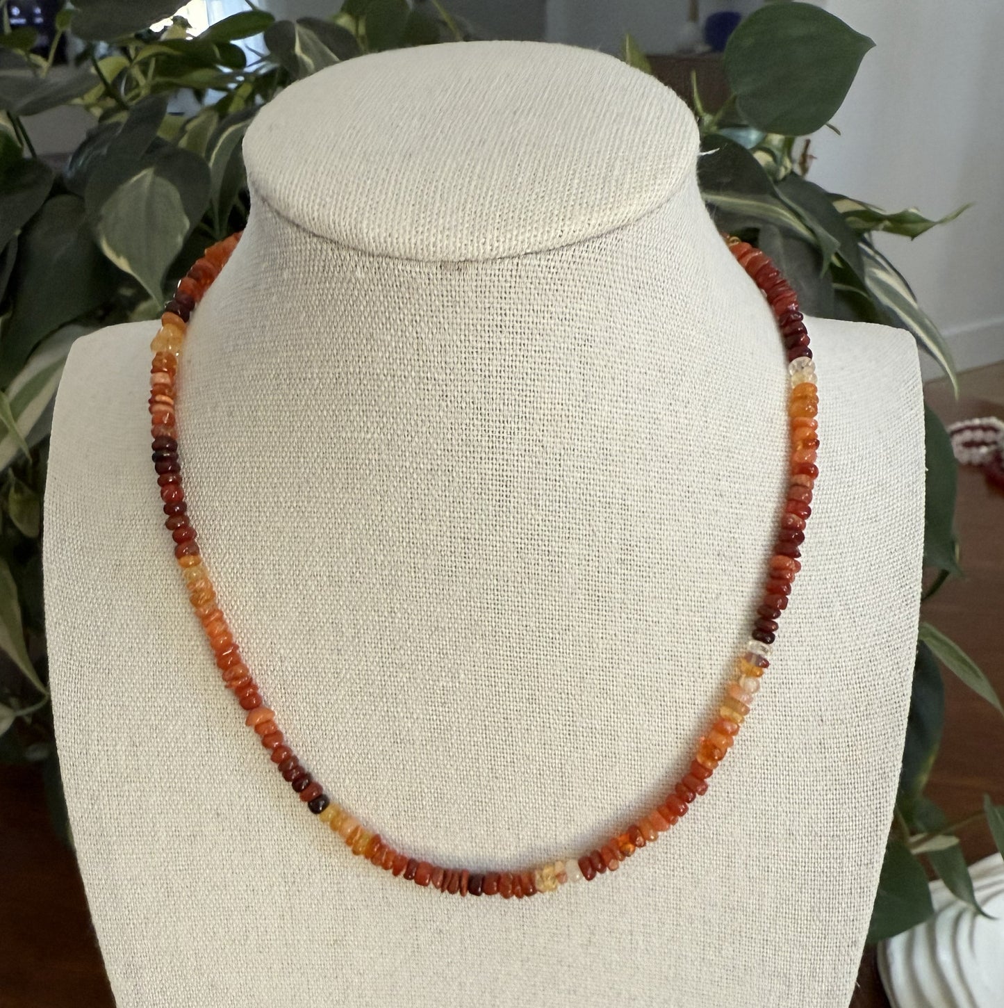 Necklace with multicolored beads on a mannequin bust against a plant background