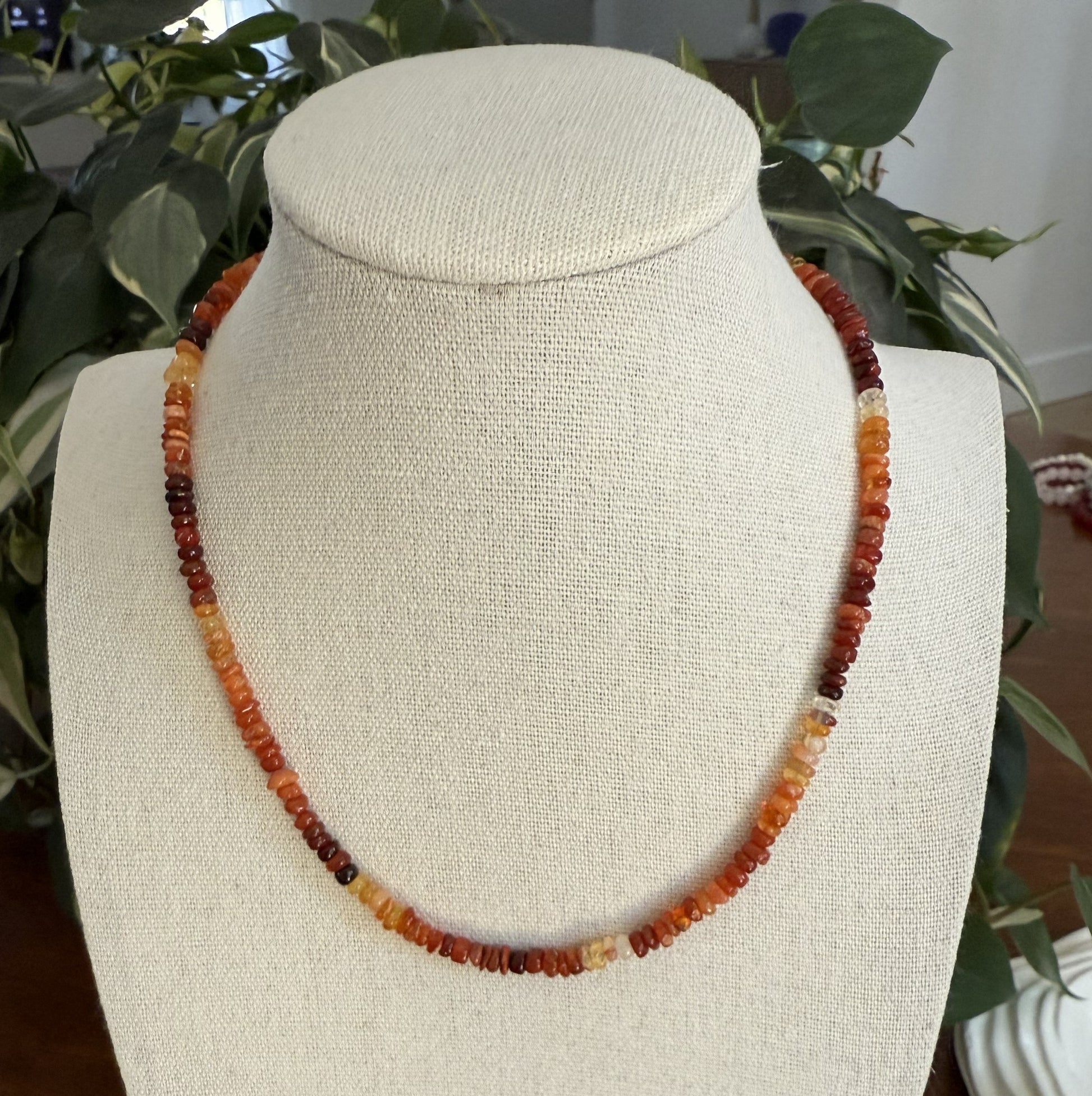 Necklace with multicolored beads on a mannequin bust against a plant background