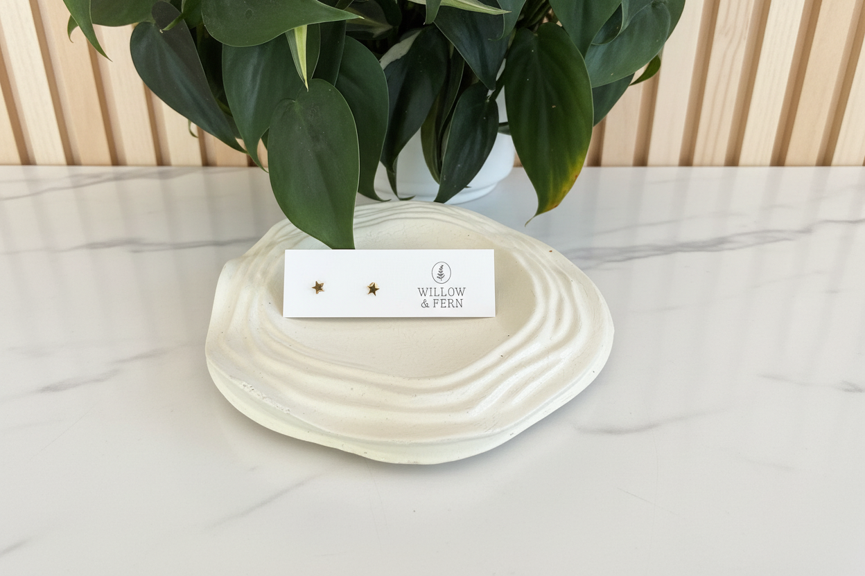 Pair of gold star earrings on a white countertop with a plant in the background