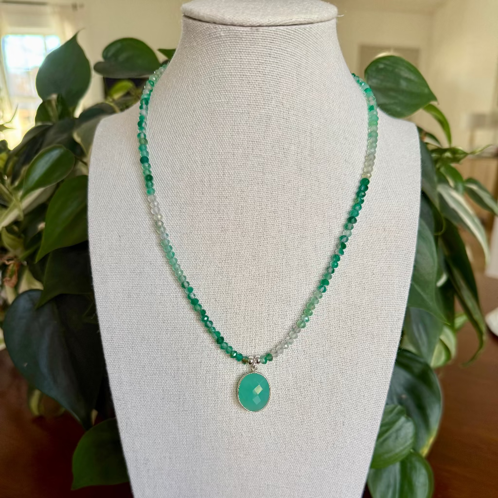 Green beaded necklace on a mannequin bust with plants in the background