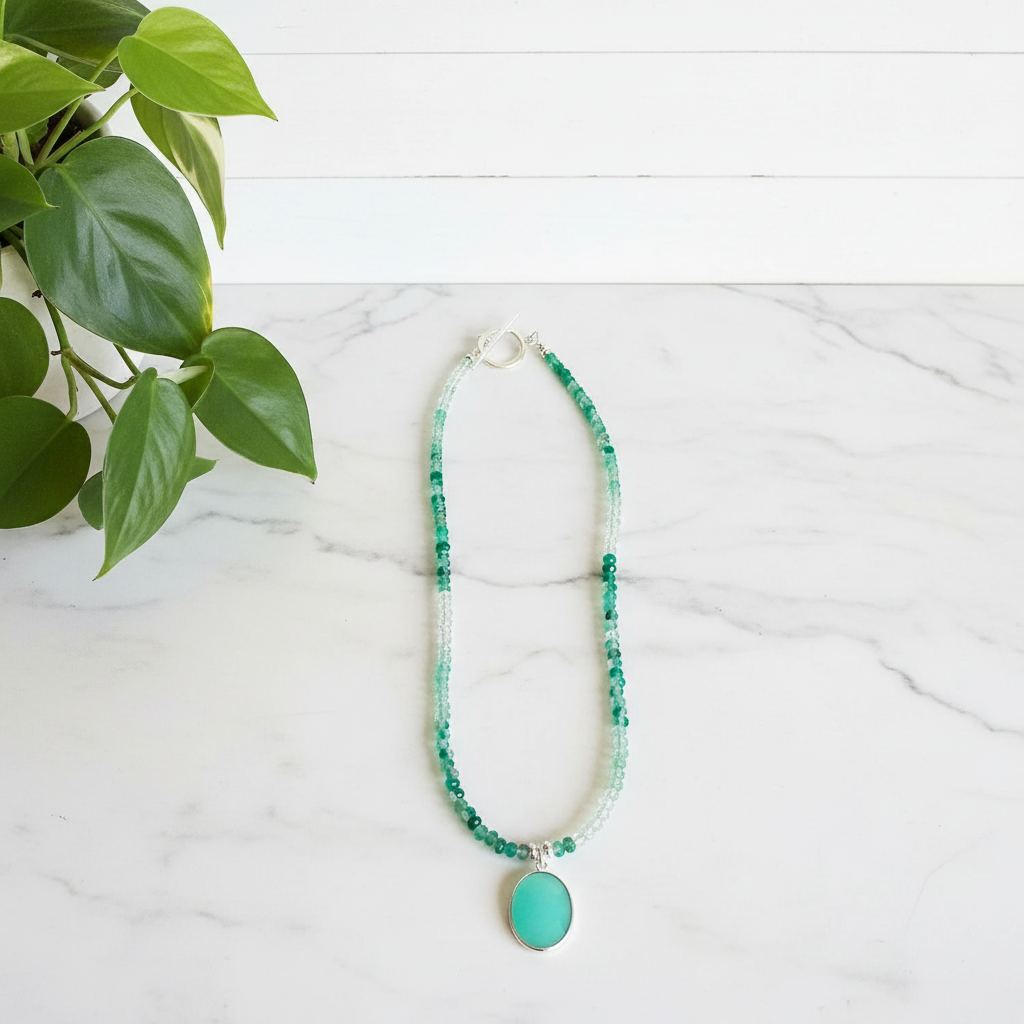 Green beaded necklace with a pendant on a white marble surface with a plant in the corner.