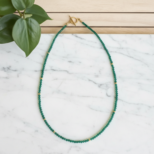 green beaded necklace on white counter with plant in background