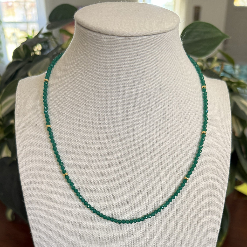 Green beaded necklace on a gray bust with a blurred indoor background