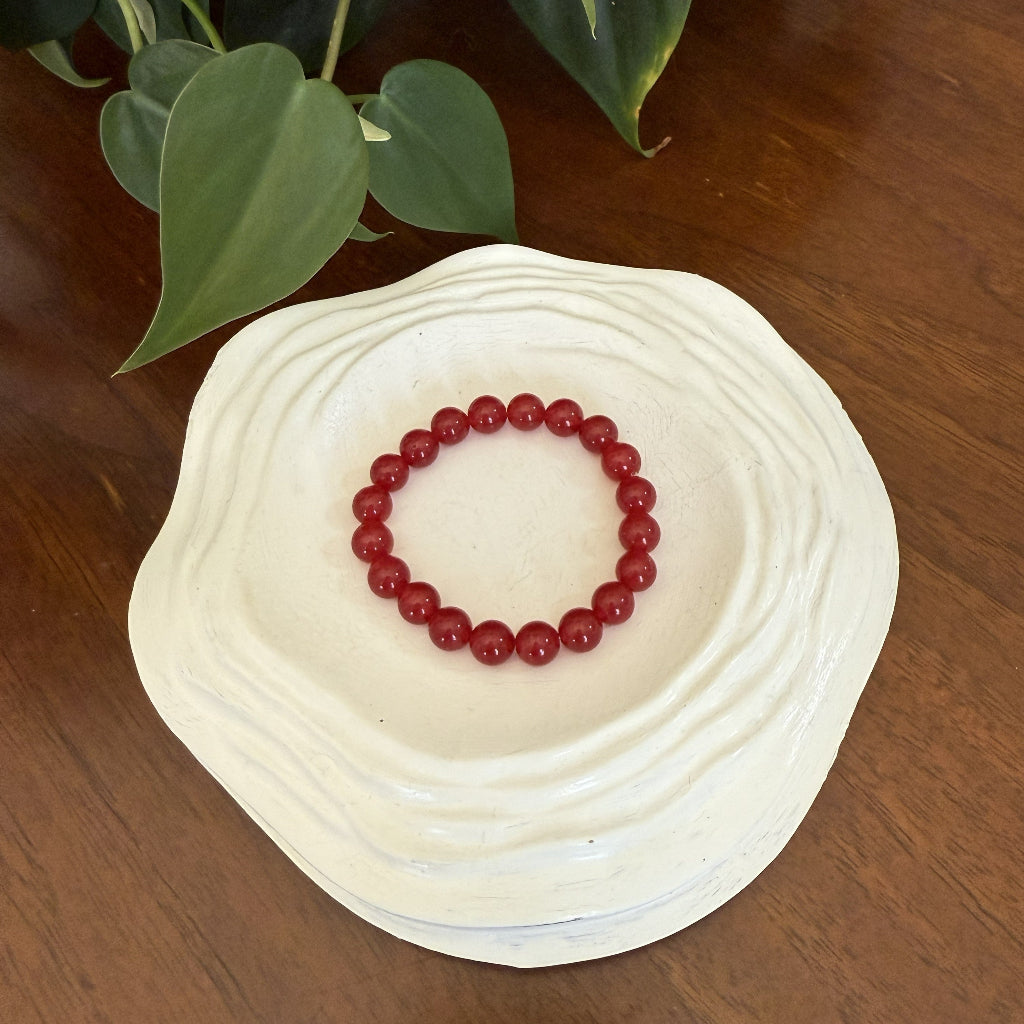 Red beaded bracelet on a white shell with green leaves in the background