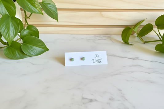 Jade earrings and a card on white counter with a plant in the background
