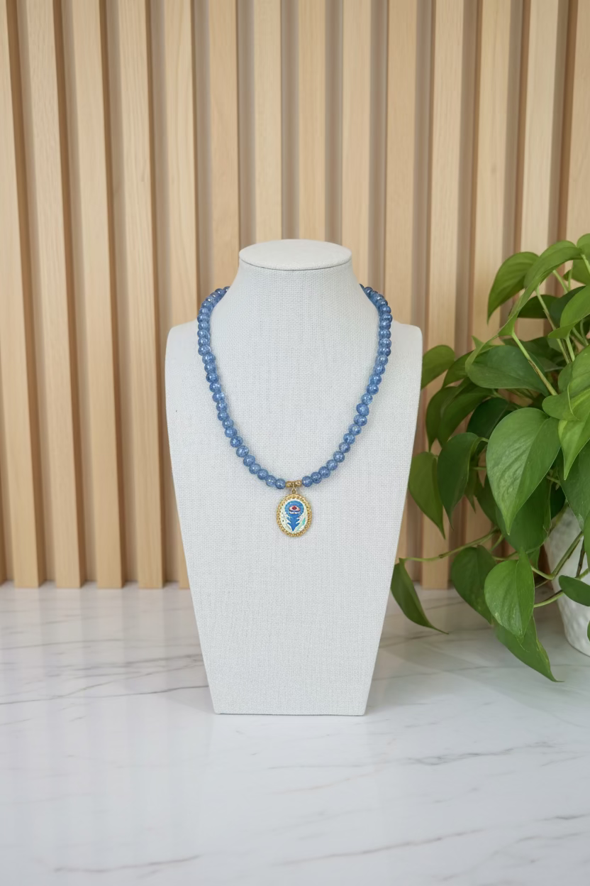 Blue beaded necklace with a pendant on a gray bust against a blurred indoor background