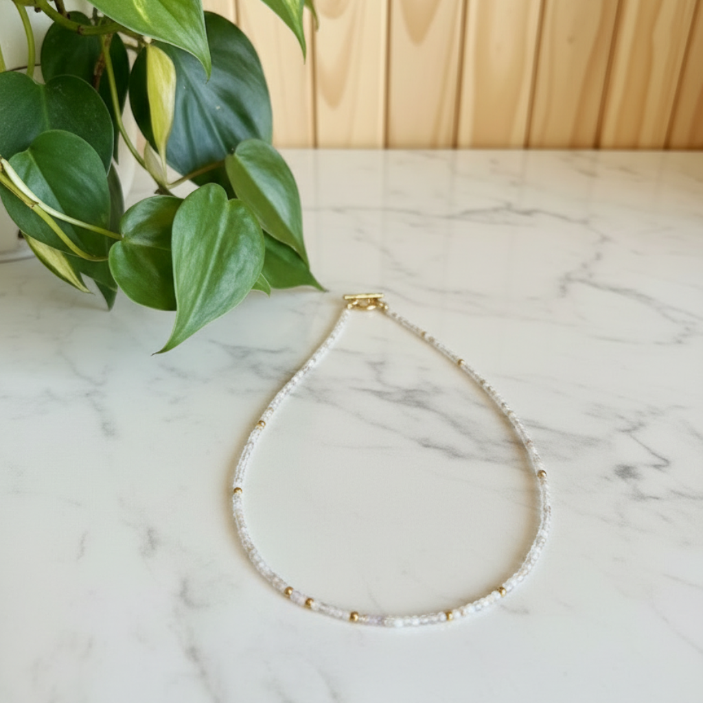 Gold necklace on a marble surface with a plant in the background