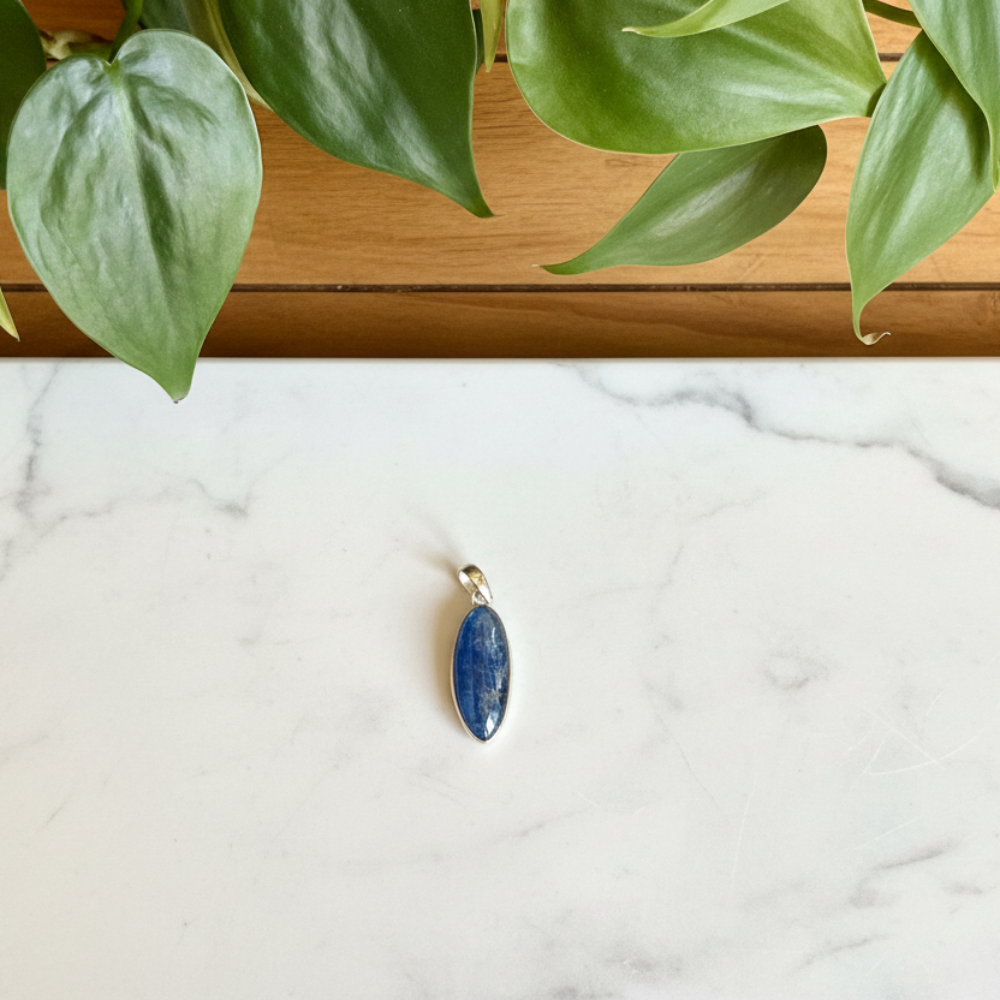 Blue kyanite pendant on a white counter with a plant in the background
