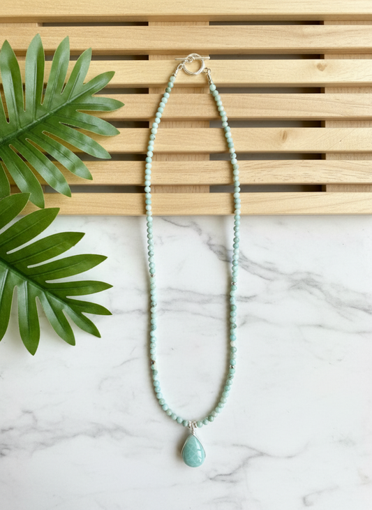 Turquoise beaded necklace with a pendant on a marble surface with a wooden slat background