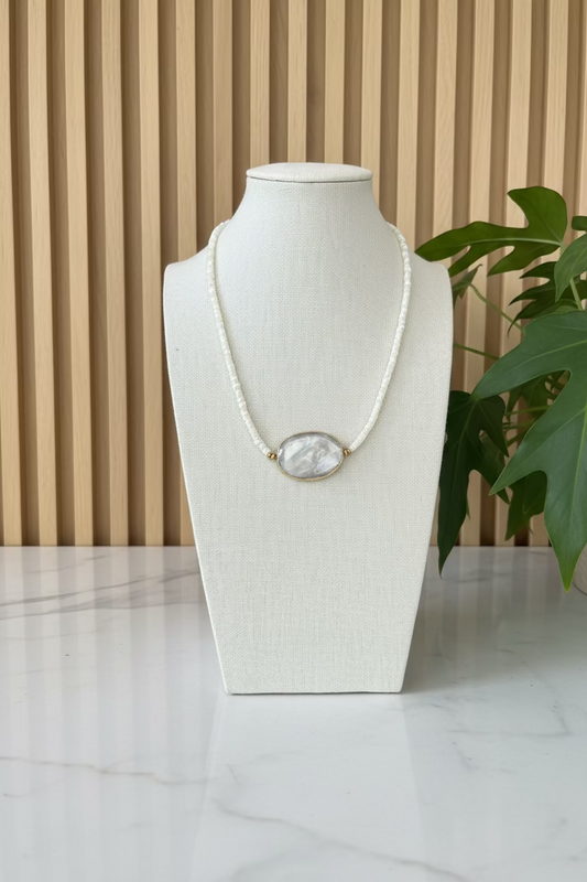 Necklace with a large central stone on a mannequin bust with plants in the background
