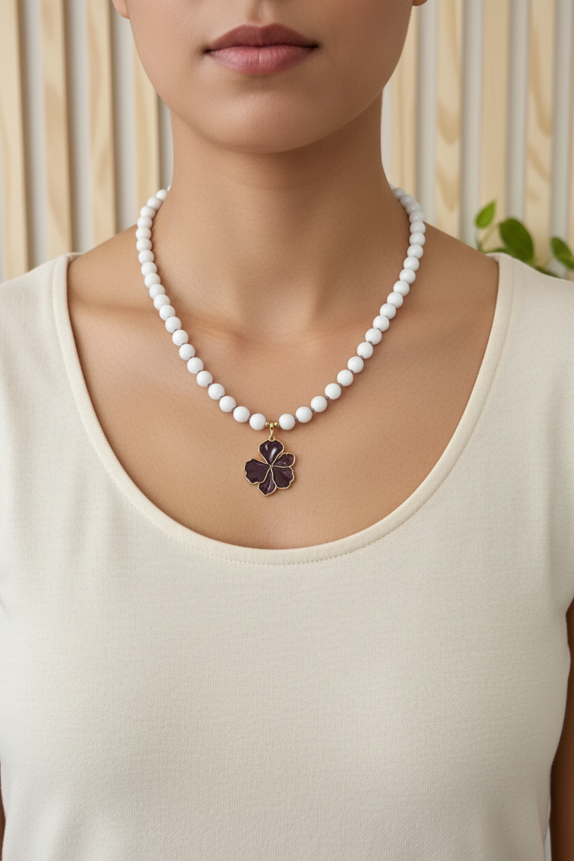 A white beaded necklace with a dark purple flower pendant on a model