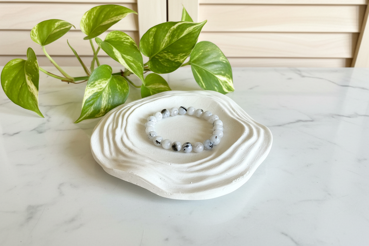 White ceramic dish with a bracelet on a marble surface, next to a green plant.