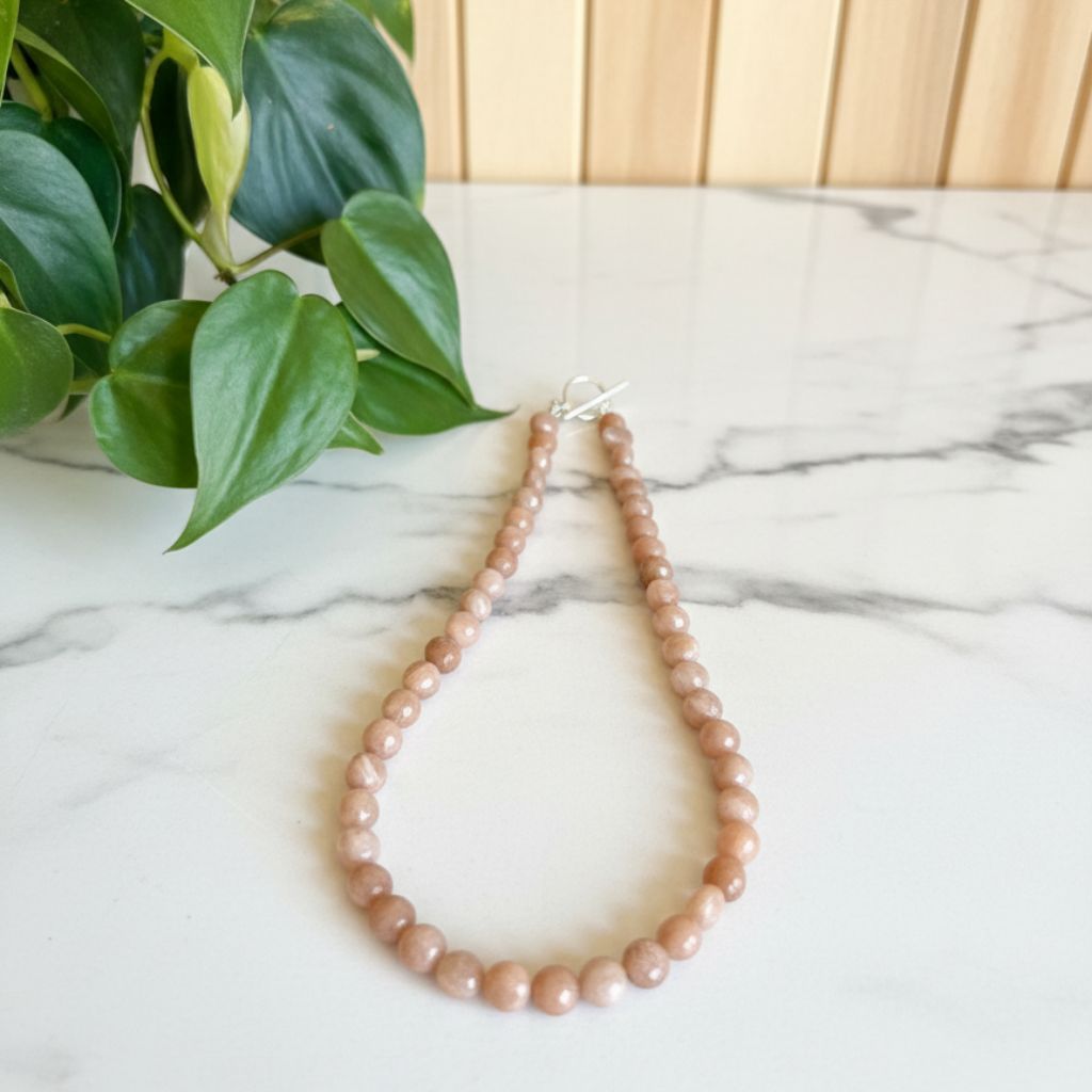 peach necklace on a white countertop with a plant in the background
