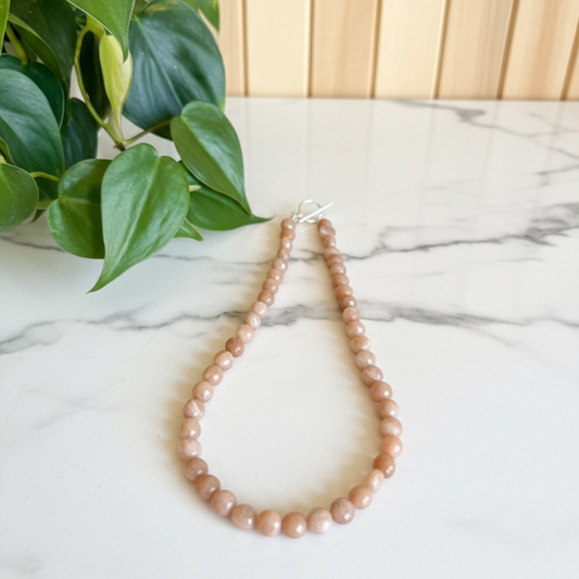 peach necklace on a white countertop with a plant in the background