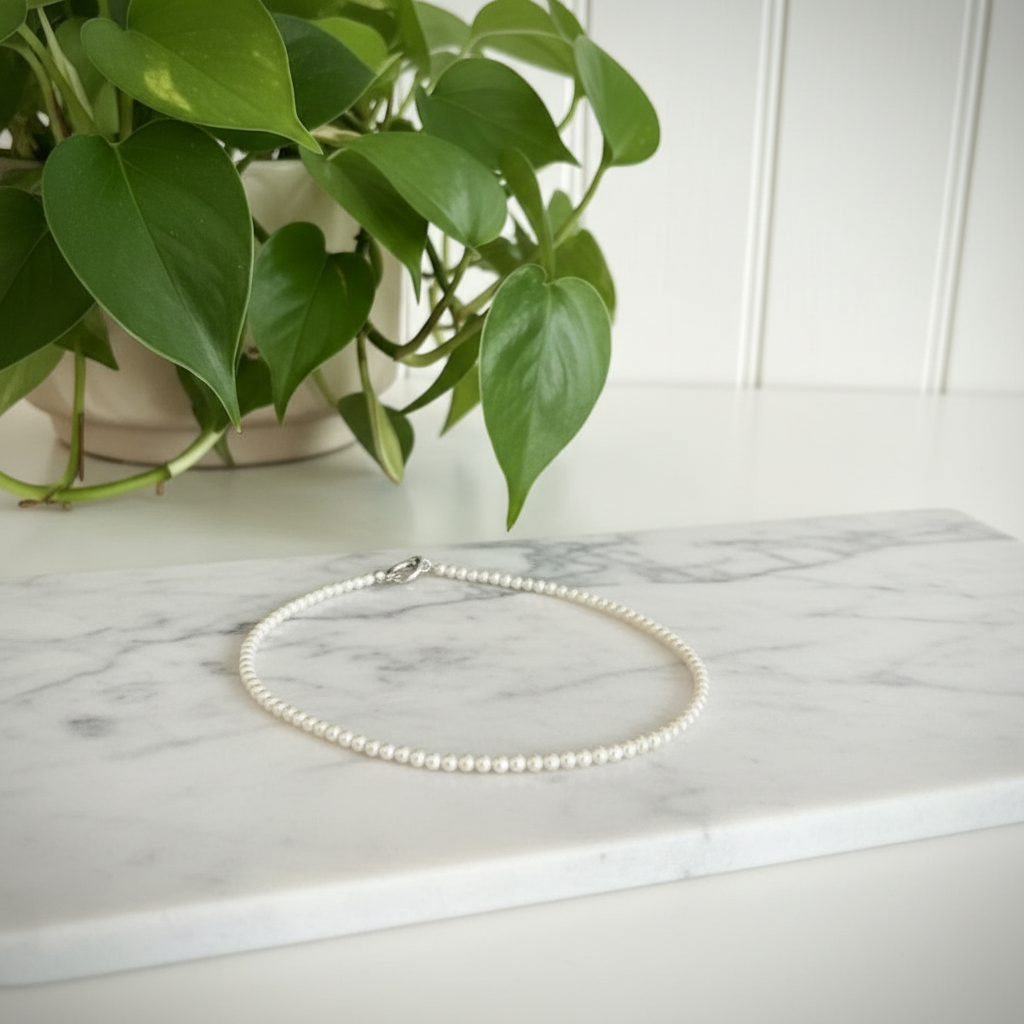 white beaded necklace on a white counter with a plant in the background
