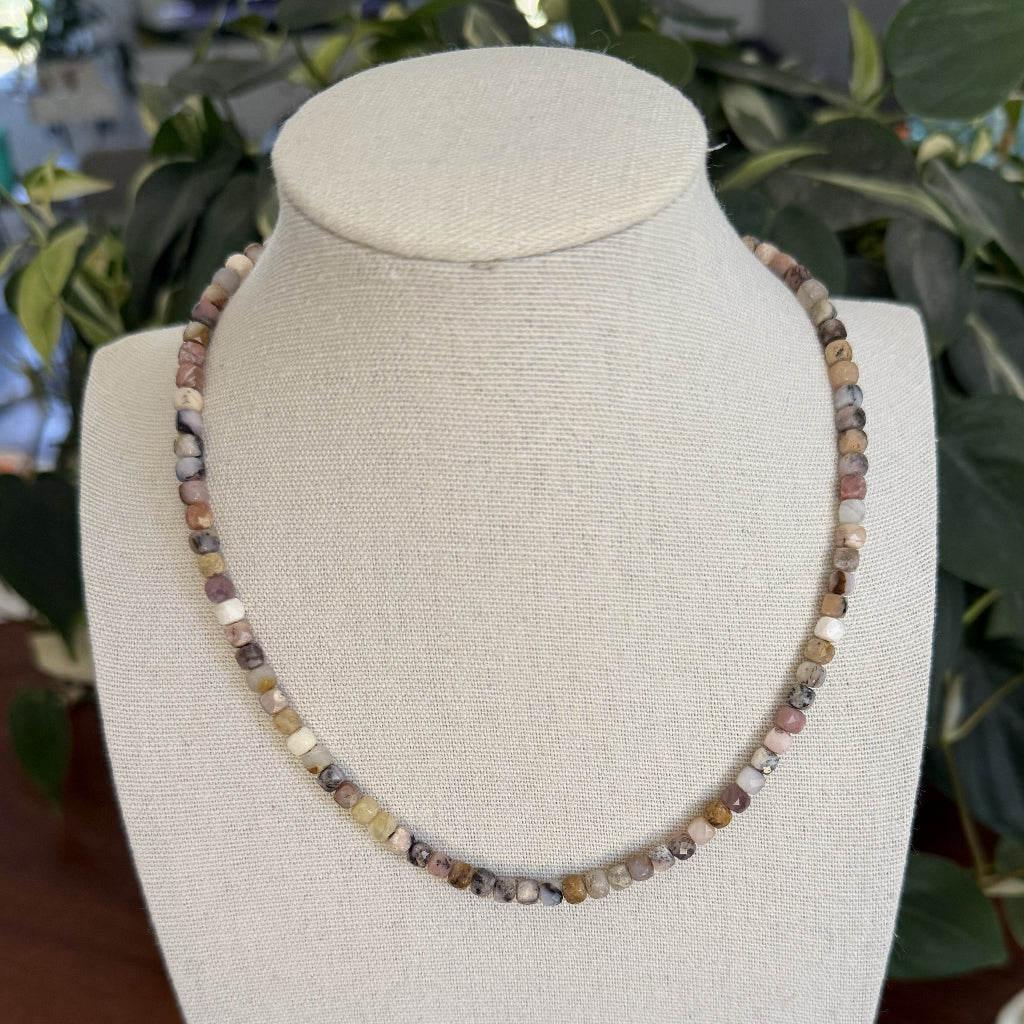 Necklace with multicolored beads on a beige bust against a blurred green plant background