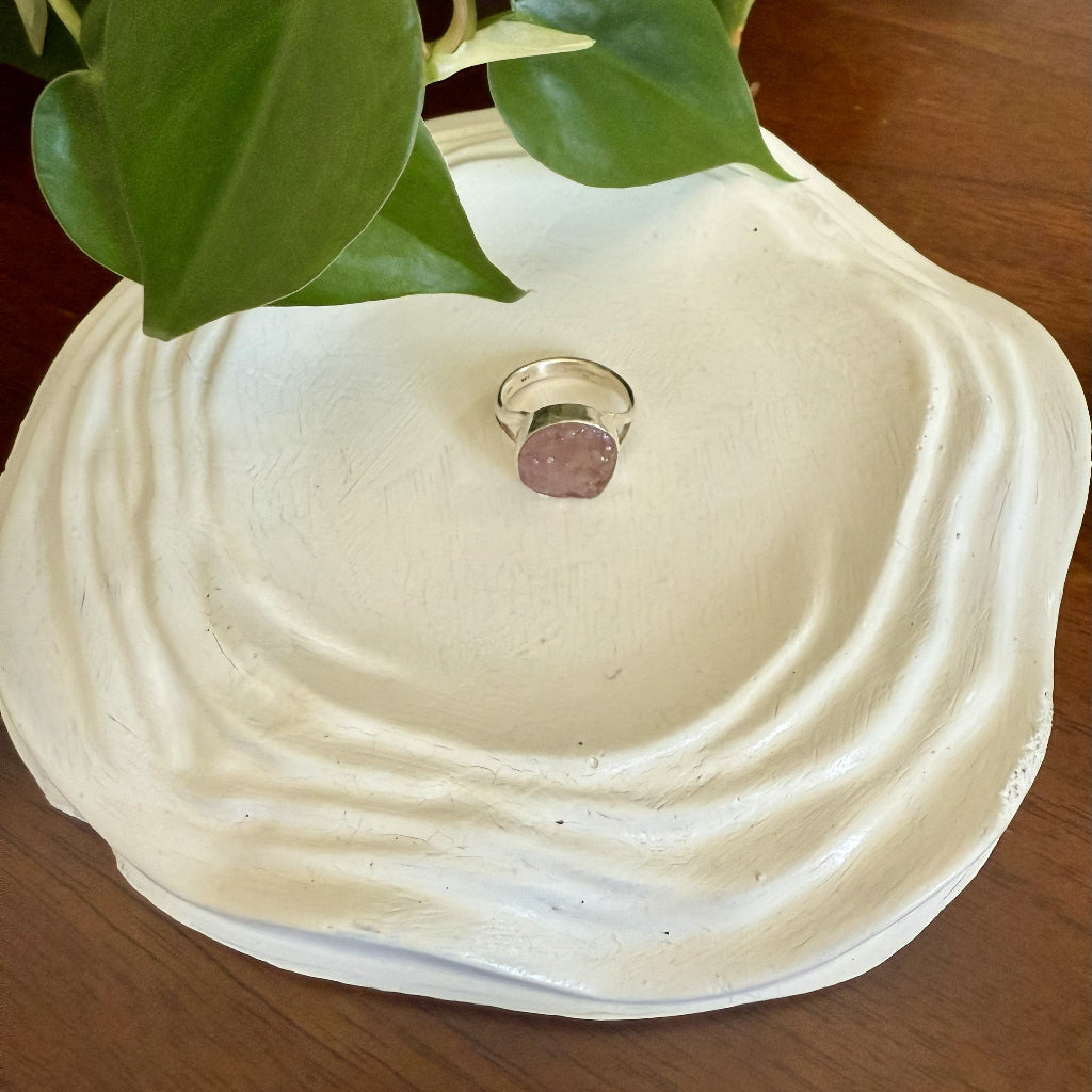 Ring on a textured white dish with green leaves in the background
