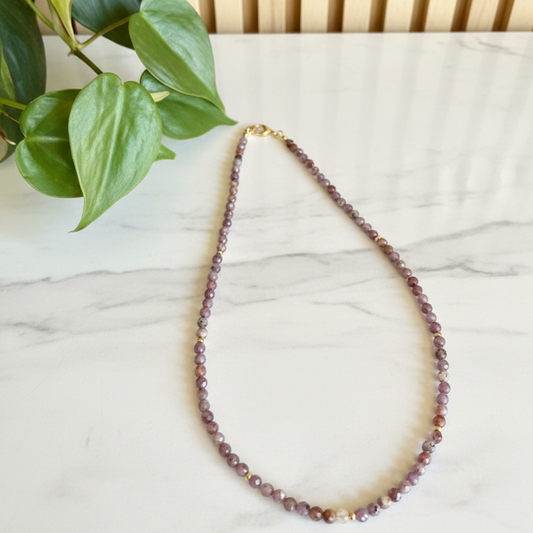 Necklace with purple beads on a marble surface with a plant in the corner