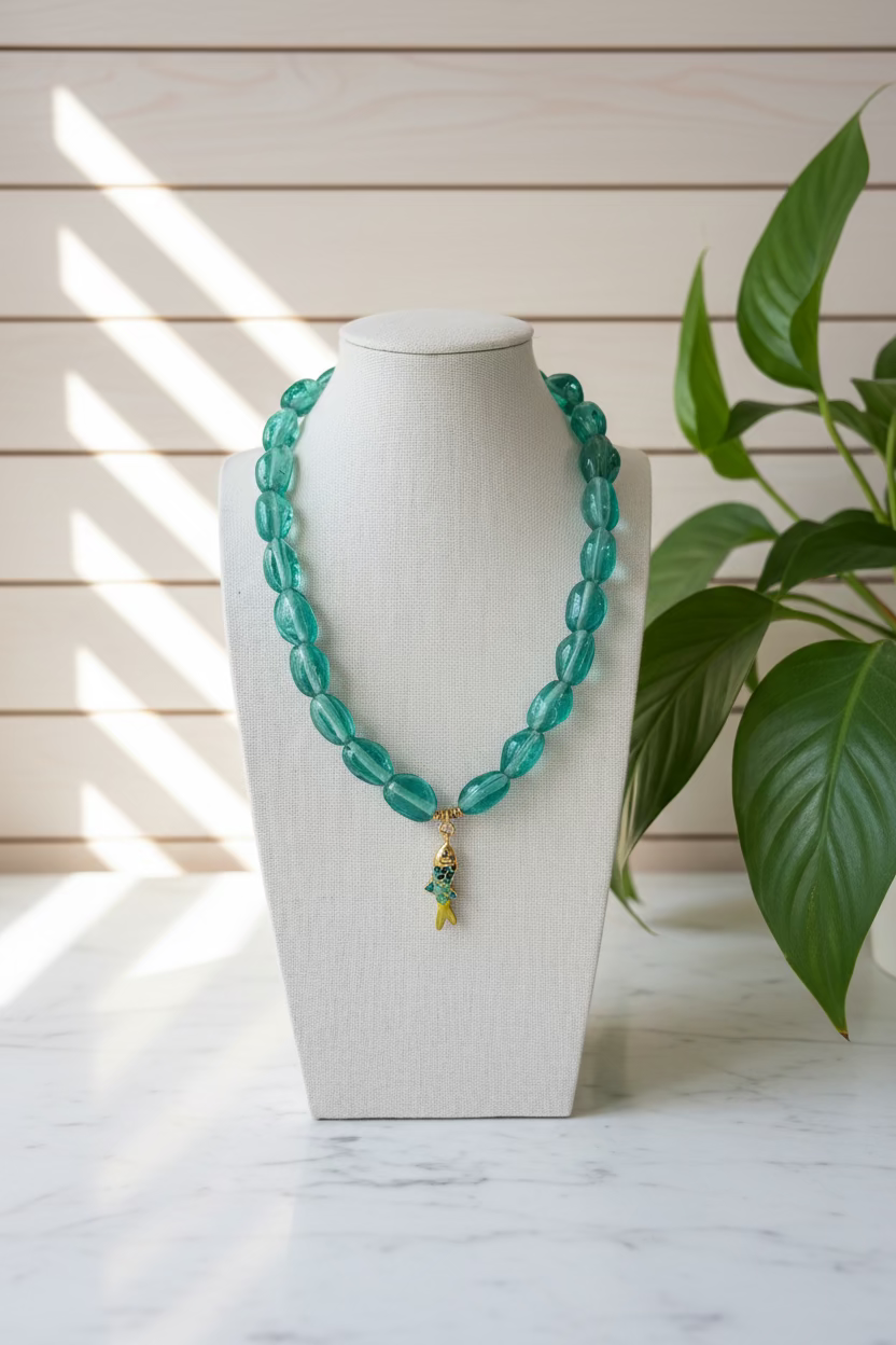Turquoise glass beaded necklace with a fish pendant on a white mannequin bust.