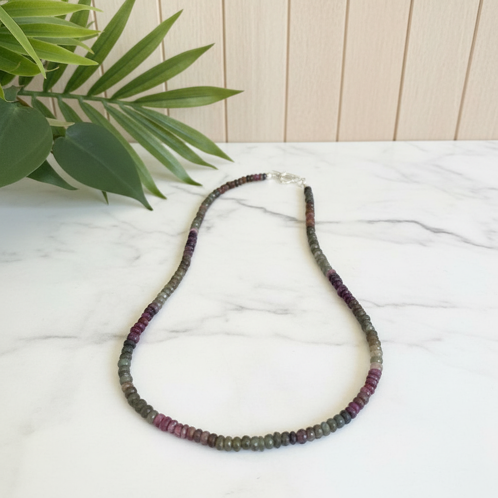 Necklace with multicolored beads on a white surface with a plant in the background