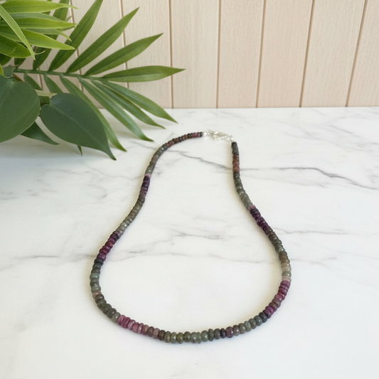 Necklace with multicolored beads on a white surface with a plant in the background