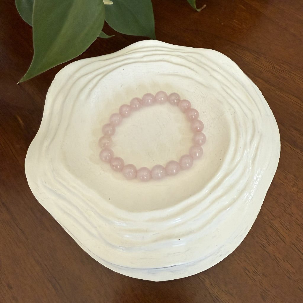 Pink beaded bracelet on a white ceramic dish with green leaves in the background