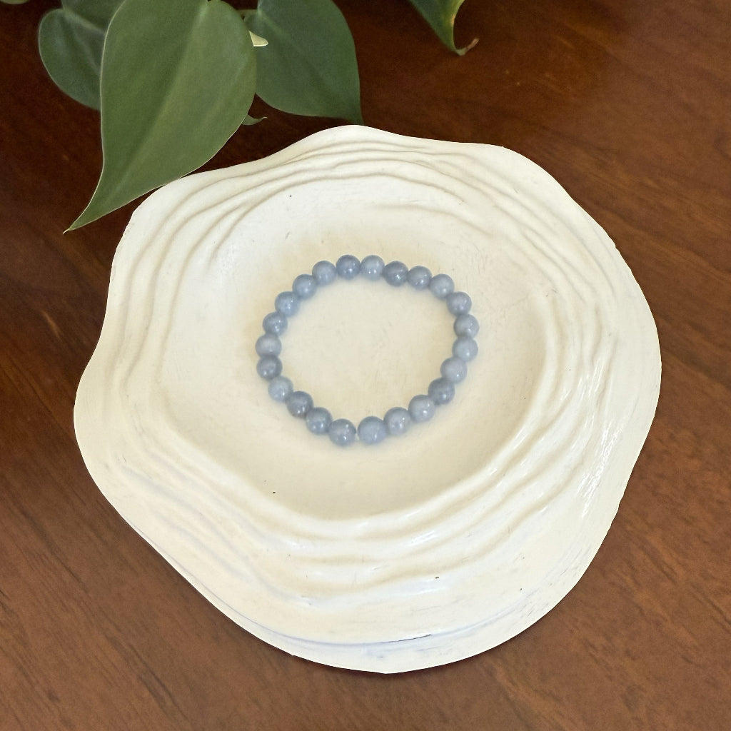Beaded bracelet on a white ceramic dish with green leaves in the background