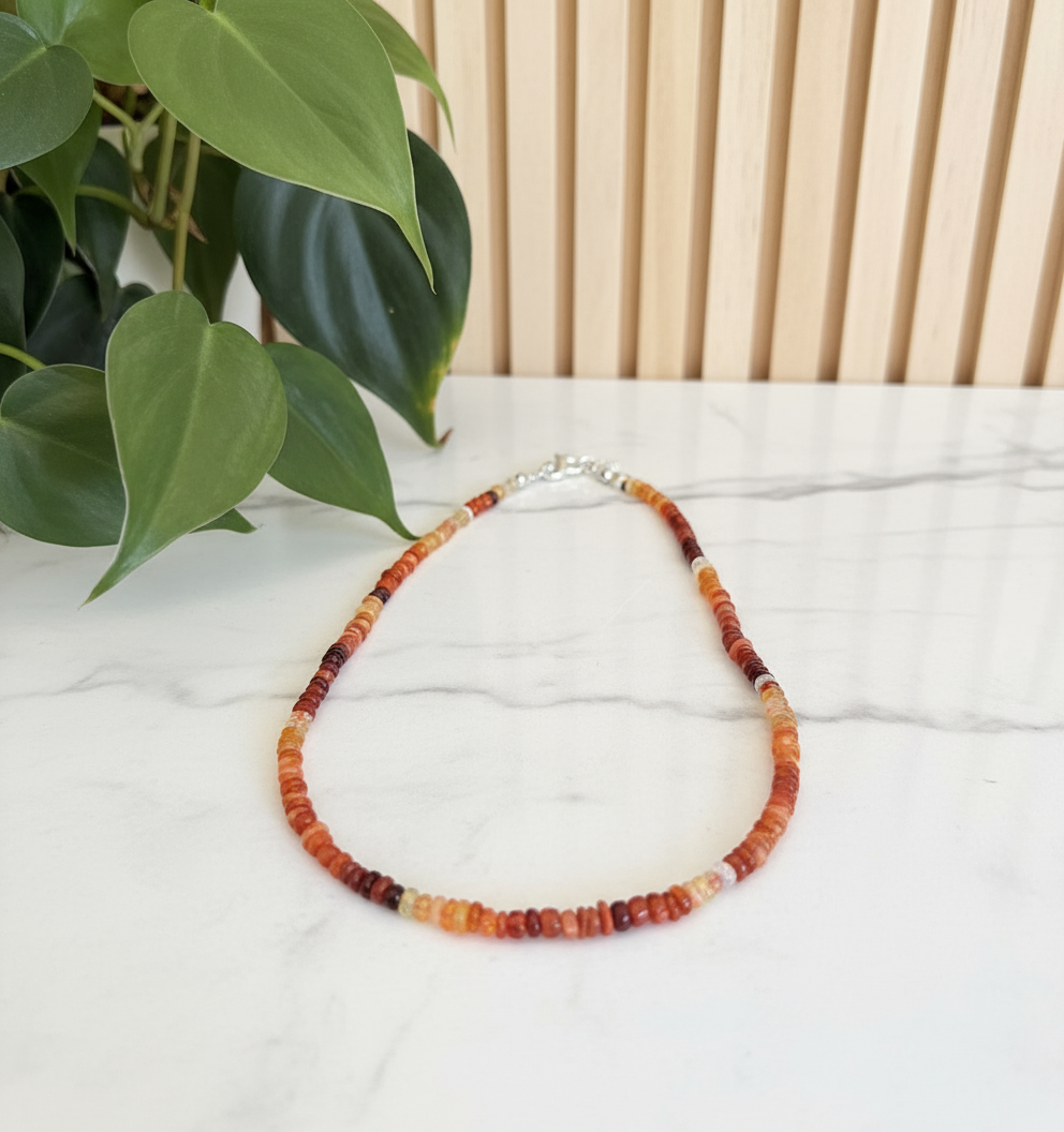 Necklace with multicolor beads on a white counter with a plant in the background