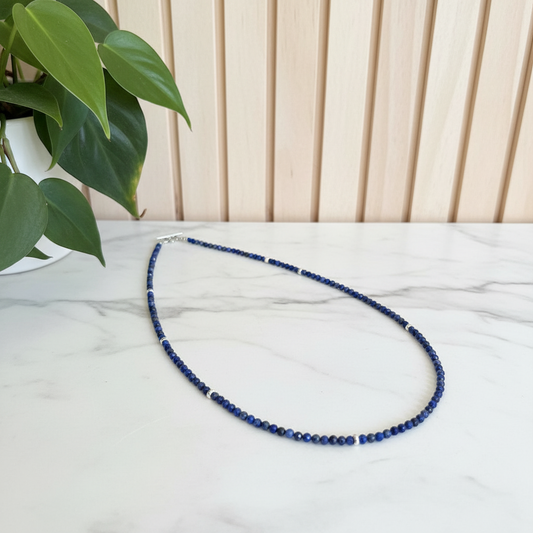 Blue beaded necklace on a white counter with green leaves in the background